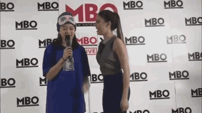 two women are standing in front of a wall with the word mbo on it .