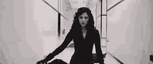 a black and white photo of a woman standing next to a man in a hallway holding a gun .