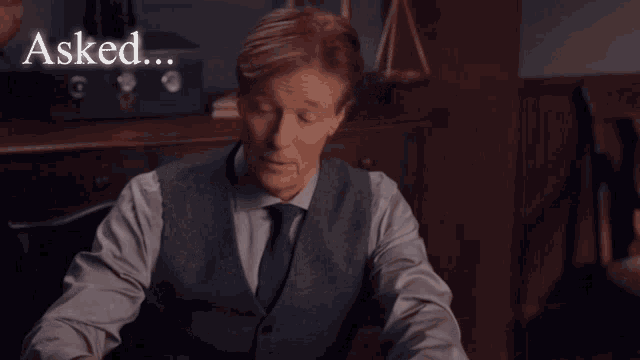 a man in a suit and tie is sitting at a table with the words " asked and answered " above him