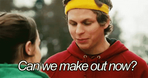a man wearing a red hoodie and a yellow headband is talking to a woman in a green shirt .