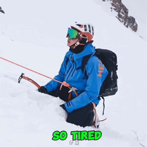 a man in a blue jacket is kneeling down in the snow with the word so tired above him