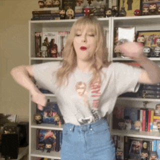 a woman wearing a star wars shirt is dancing in front of a bookshelf filled with pop figures