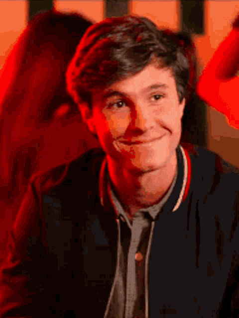 a young man is smiling and looking at the camera while wearing a blue jacket .