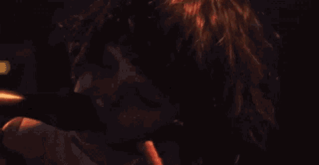 a woman is singing into a microphone in a dark room while wearing a choker .