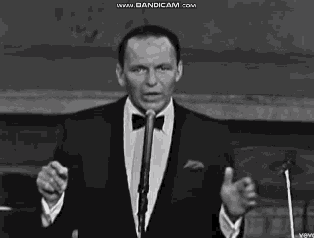 a man in a tuxedo is singing into a microphone with the website www.bandicam.com visible