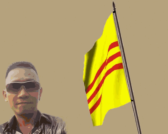 a man in sunglasses stands in front of a yellow flag with red stripes