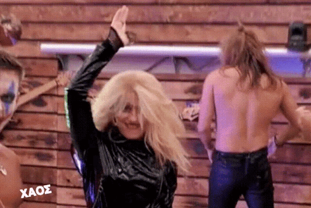 a group of people are dancing in front of a wooden wall with the word xaos on the bottom right