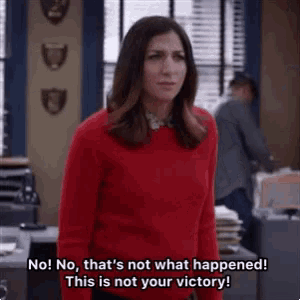 a woman in a red sweater is standing in an office and saying no that 's not what happened this is not your victory