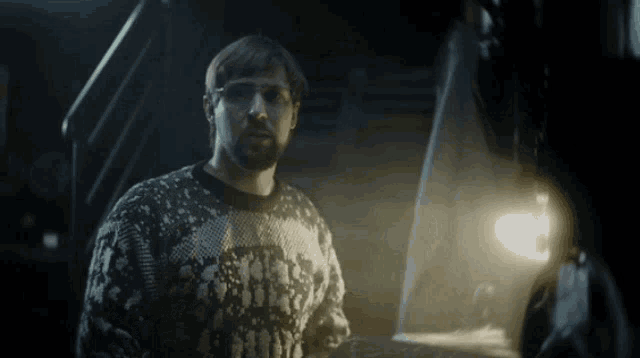 a man wearing a batman sweater stands in front of a statue