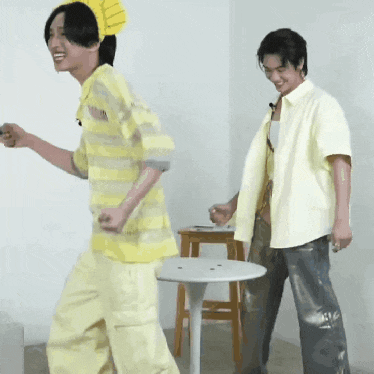 two young men are dancing in a room next to a table .