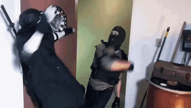 a man wearing a mask is standing in a room with a mop and a barrel