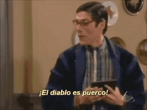a man in a blue jacket is holding a cell phone and says el diablo es puerco .