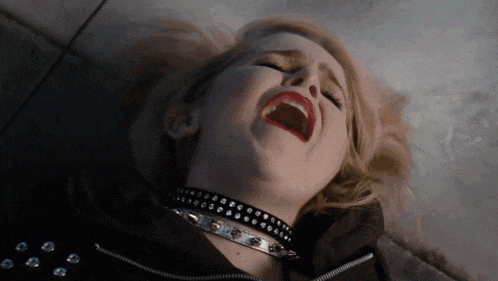 a woman wearing a choker and a black jacket is laying on the ground with her mouth open