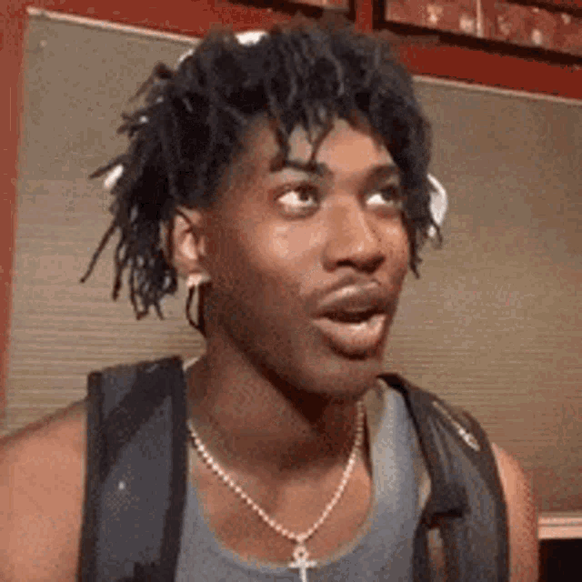 a man with dreadlocks is wearing a backpack and a necklace with an ankh on it .