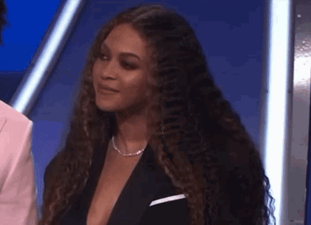 a woman with long curly hair is wearing a tuxedo and a pink jacket .