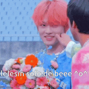 a man with pink hair is holding a bouquet of flowers and another man is touching his face .