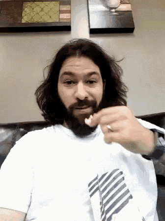 a man with long hair and a beard is eating popcorn on a couch