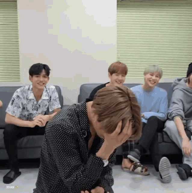 a group of young men are sitting on a couch and one has his hand on his face