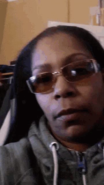 a woman wearing sunglasses and a green hoodie looks at the camera