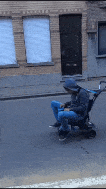 a man in a hoodie sits in a stroller on a street