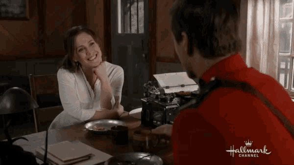 a man in a red uniform is sitting at a table with a woman in a white shirt and the words hallmark channel on the bottom