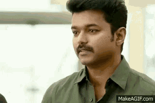a man with a mustache is wearing a green shirt and looking at something .