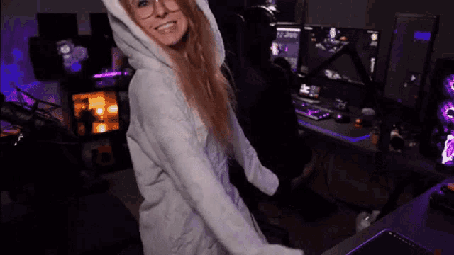 a woman in a white hoodie is standing in front of a computer in a room .
