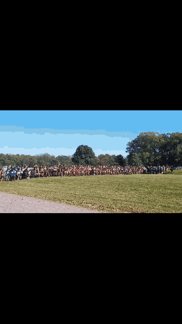 a group of runners are running on a grassy field . one of the runners has the number 1955 on his jersey .