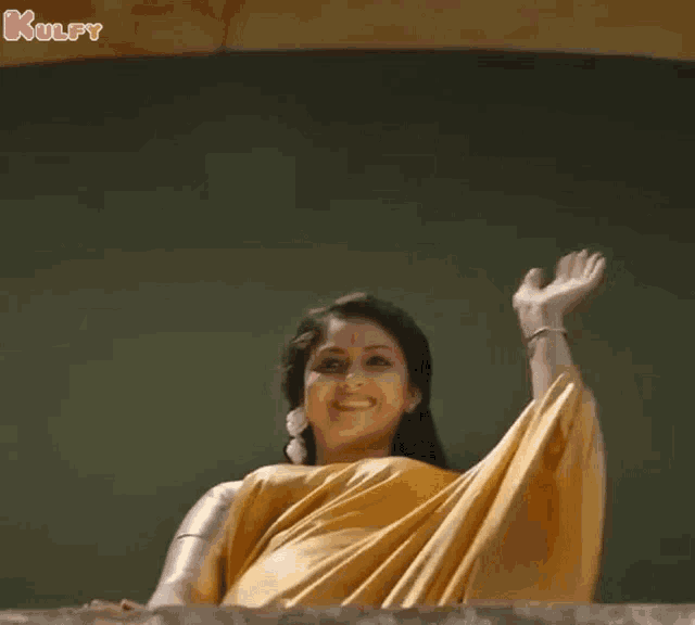 a woman in a yellow saree is waving her hand