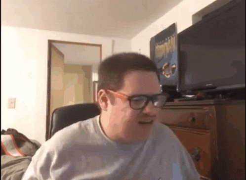 a man wearing glasses is sitting in a chair in front of a tv .
