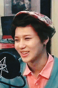 a young man wearing a hat and a pink shirt smiles in front of a microphone