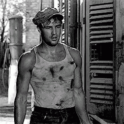 a man in a tank top and hat is standing in front of a building in a black and white photo .