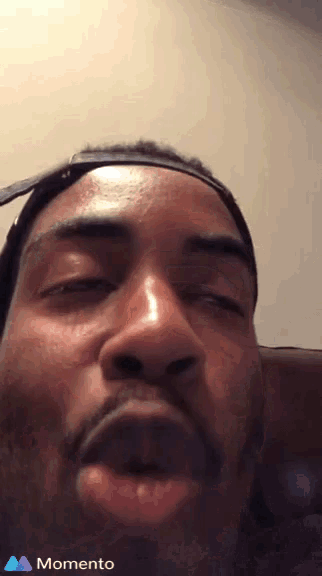 a close up of a man 's face with a momento logo on the bottom right