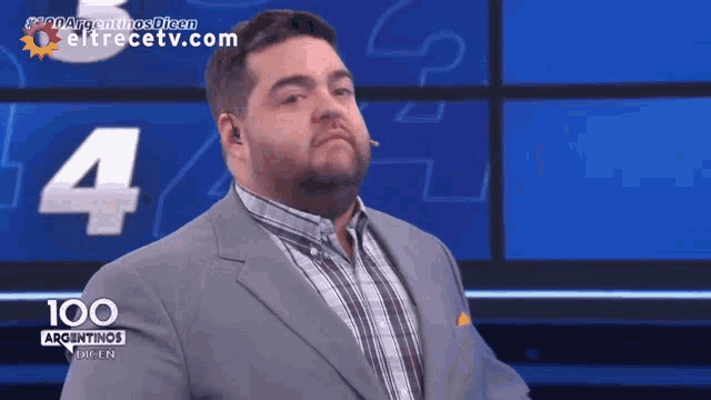 a man in a suit and plaid shirt stands in front of a screen that says 100 argentinas
