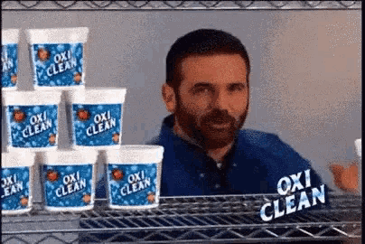 a man with a beard is standing in front of a shelf filled with oxi clean containers .