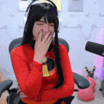 a woman wearing headphones and a red shirt is covering her mouth with her hand .