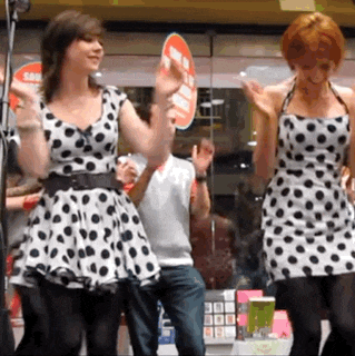 two women in polka dot dresses are dancing in front of a store window