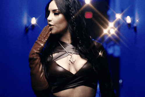 a woman in a leather top and gloves stands in front of a blue background