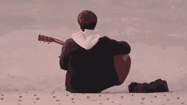 a man is sitting on the beach with a guitar .