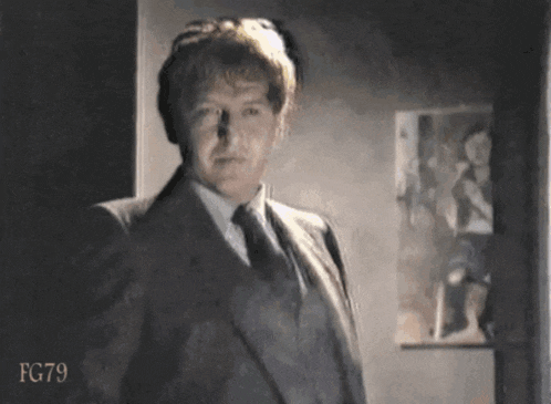 a man in a suit and tie is standing in front of a wall with fg79 written on the bottom
