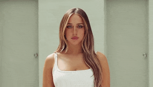 a woman in a white tank top is standing in a hallway between two doors .