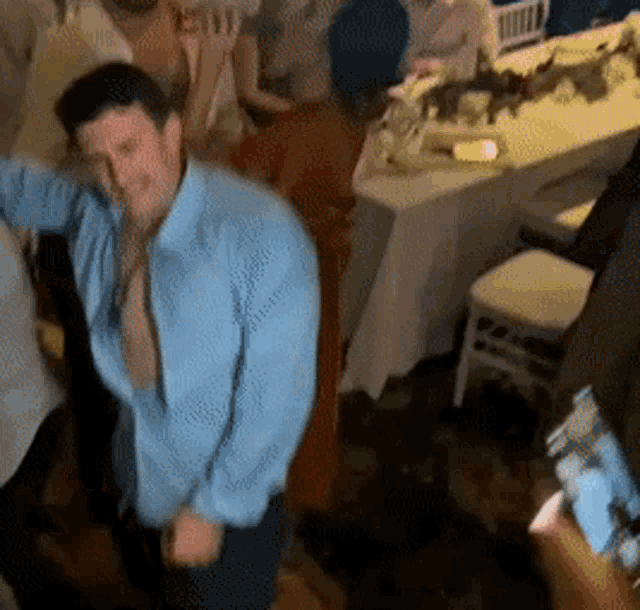 a man in a blue shirt is dancing in a room with other people