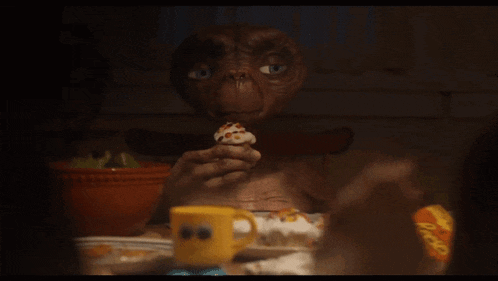 an alien is sitting at a table eating cupcakes and a cup of reese 's peanut butter cups