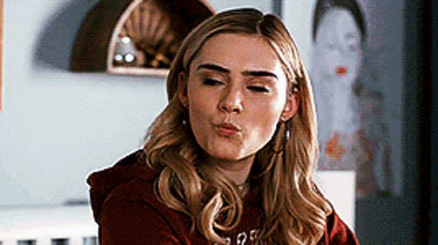 a woman in a red hoodie is making a funny face in front of a painting .