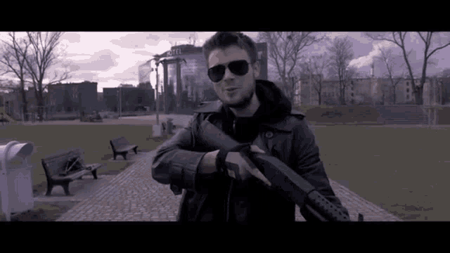 a man in sunglasses holds a shotgun in front of a hotel