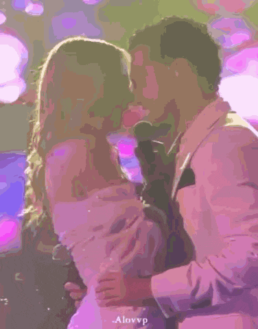 a man in a suit is holding a woman in a white dress and kissing her .