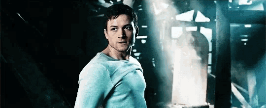 a man in a blue shirt is standing in a dark room with a light shining through the ceiling .