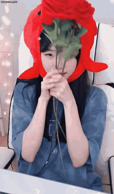 a girl wearing a red octopus hat holds a red rose in front of her face