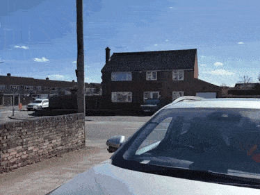 a white car is parked in front of a brick wall and a house