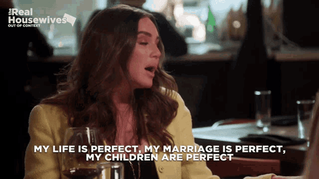 a woman is sitting at a table with a glass of wine and says her life is perfect her marriage is perfect and her children are perfect